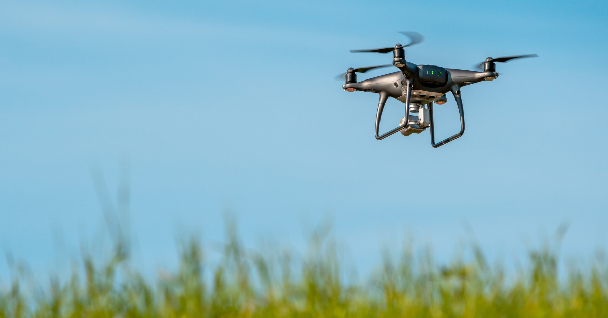 Drone quadcopter hovering over grass field on sunny day [Canva License]